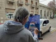 DEÁN FUNES: RUBÉN ROQUE RAMÍREZ LLENÓ DE COLOR LA CALLE 25 DE MAYO PINTANDO AL AIRE LIBRE EL LAPACHO ROSADO DE BANCO CÓRDOBA.