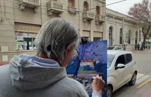 DEÁN FUNES: RUBÉN ROQUE RAMÍREZ LLENÓ DE COLOR LA CALLE 25 DE MAYO PINTANDO AL AIRE LIBRE EL LAPACHO ROSADO DE BANCO CÓRDOBA.